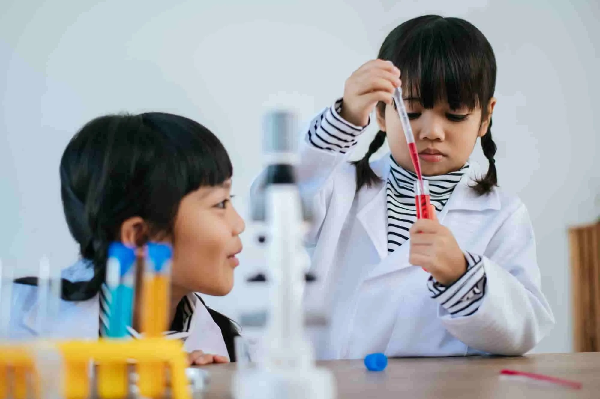 Two young children in lab coats experimenting with a test tube, fostering curiosity and cognitive skills.