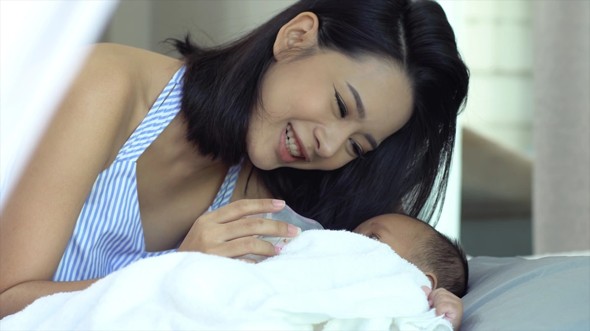 Mother smiling at baby on bed.
