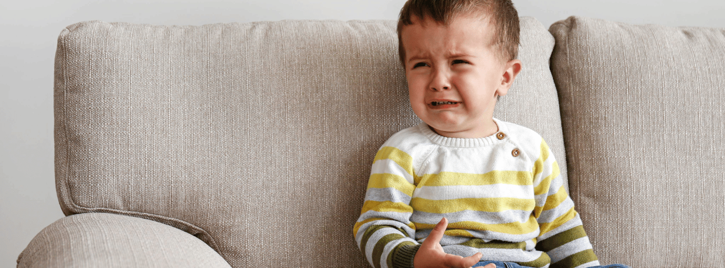 Niño pequeño llorando en el sofá, representando malestares gastrointestinales leves comunes en la infancia.