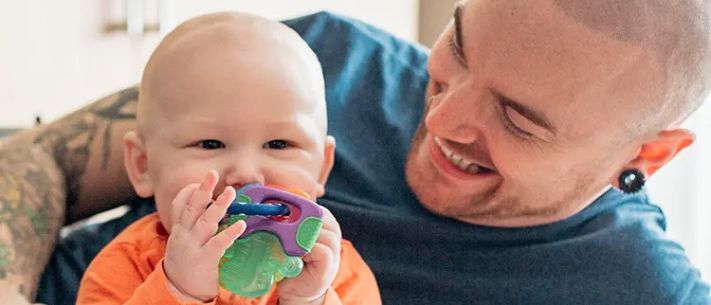Baby sucking on pacifier as dad watches in enjoyment
