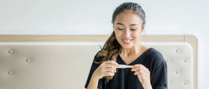 Woman smiling and holding pregnancy test on bed 