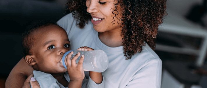 Mother With Curly Brown Hair Feeding Her Baby With Bottle