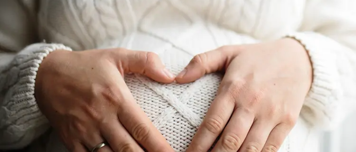 Close-up of pregnant woman making a heart shape with her hands rested on belly