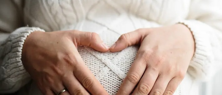 Close-up of pregnant woman making a heart shape with her hands rested on belly