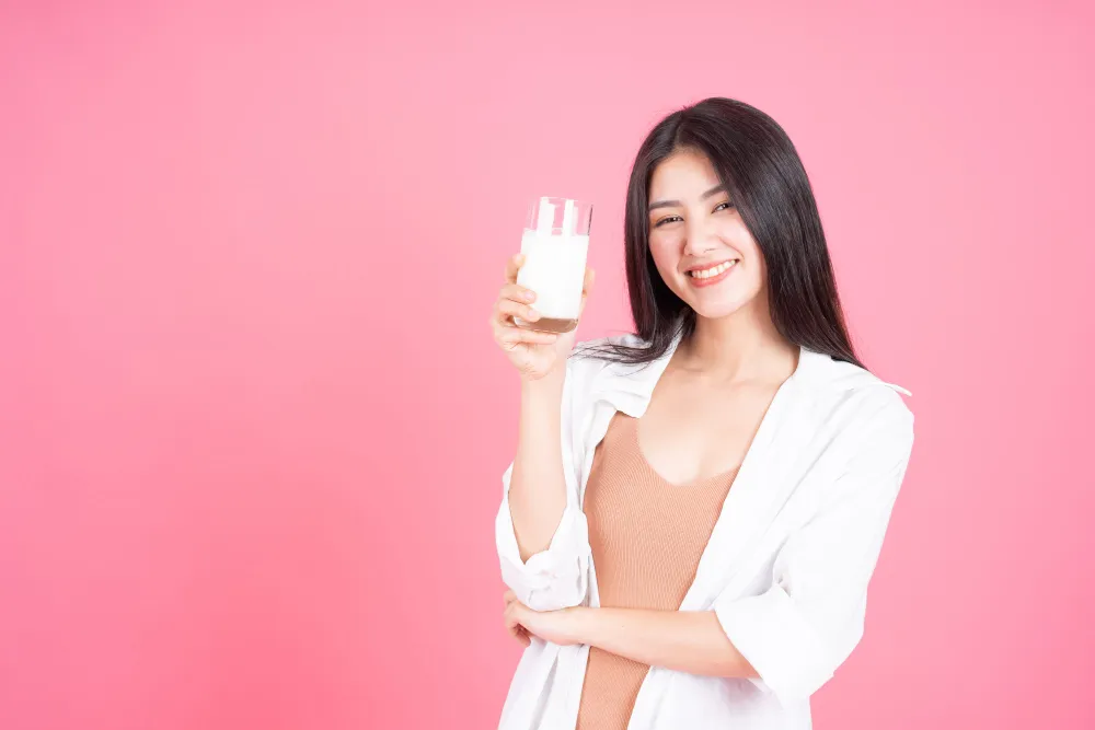 Woman smiling while holding a glass of milk against a pink background