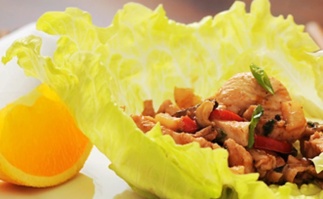 Lettuce wrap dish with an orange slice served on white platter