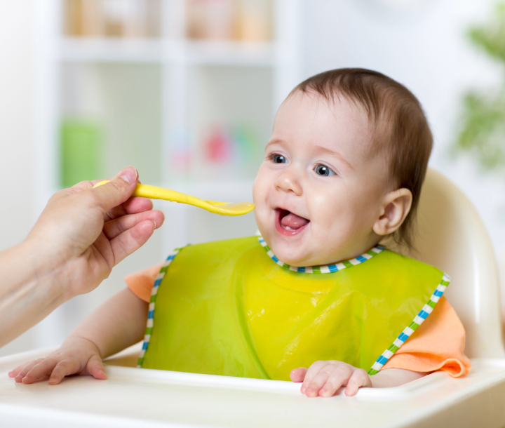 Bebé abriendo la boca para recibir una cucharada de comida, acompañado de texto sobre el calendario de alimentación infantil.