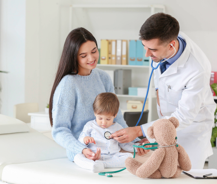 Pediatra examinando a un bebé en presencia de su madre, ilustrando el diagnóstico y tratamiento de la APLV.