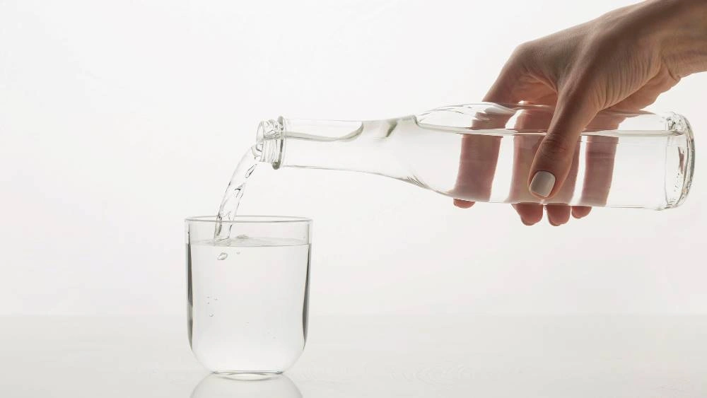 Hand Pouring Clear Water From A Bottle Into A Glass