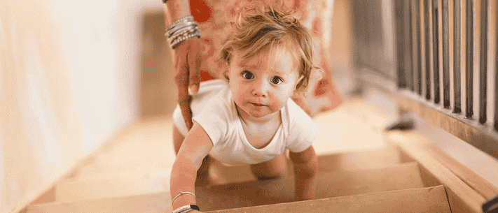 Toddler Crawling Up Wooden Stairs with a Hand on Back, Floral Garment Partially Visible