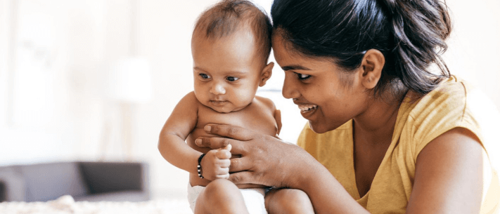 Smiling Mother Holding Baby in Bright Room