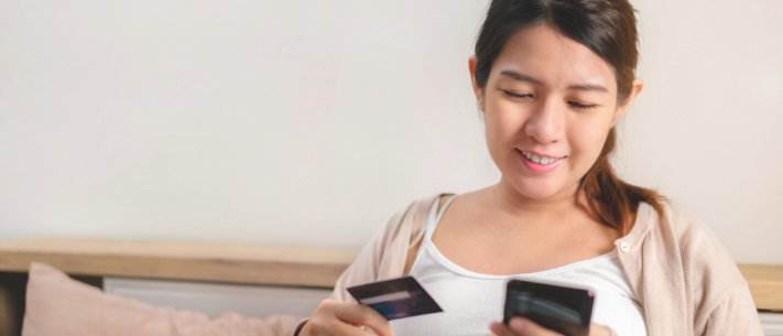 Pregnant woman shopping online with phone while holding credit card