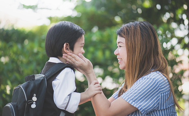 Mother In Blue And White Striped Shirt Touching Her Son's Face Outdoors With Green Background