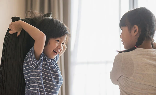Young boy and girl siblings playing pillow fight 