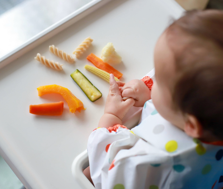 Bebé sentado en su silla observando alimentos saludables, representando el impacto del DHA y ARA en el desarrollo mental.