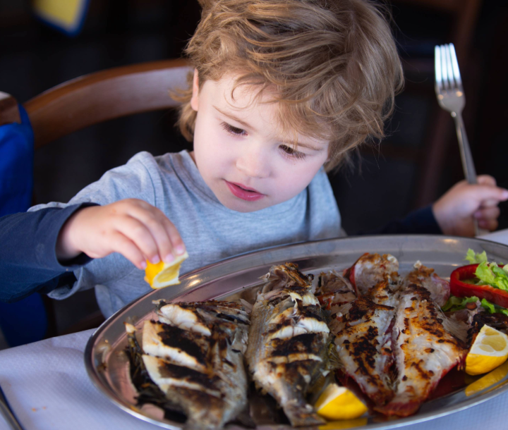 Niño pequeño disfrutando un plato con pescado, fuente natural de DHA para el desarrollo cerebral.