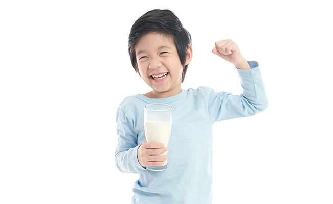 Young boy in blue sleeves holding a glass of milk smiling with one arm flexing against white background