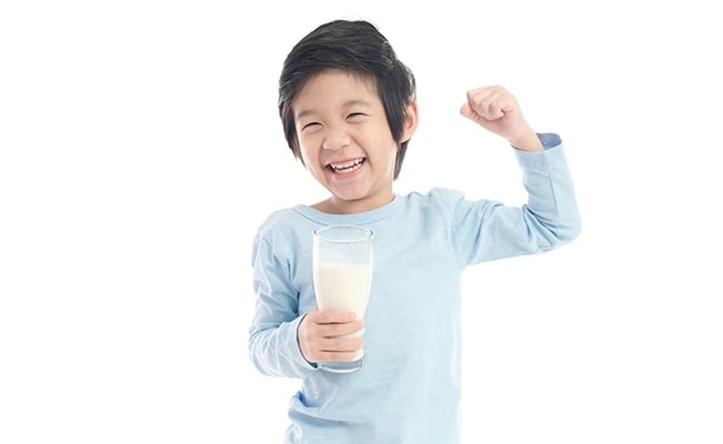 Young boy in blue sleeves holding a glass of milk smiling with one arm flexing against white background
