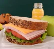 Sandwich served with fruits and orange juice in bottle.