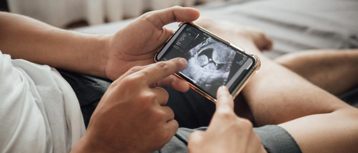 Close-up of male pair of hands holding phone displaying ultrasound picture while a female hand points on the screen