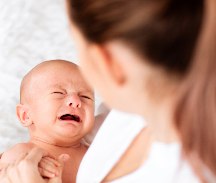 Bebé llorando mientras es sostenido por un adulto, acompañado de texto sobre la irritabilidad, los cólicos y el llanto frecuente en la infancia.