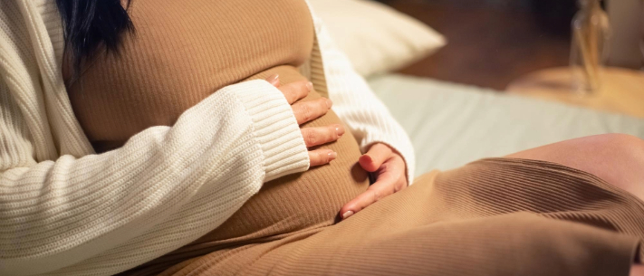 Close-up of woman holding belly while sitting on sofa