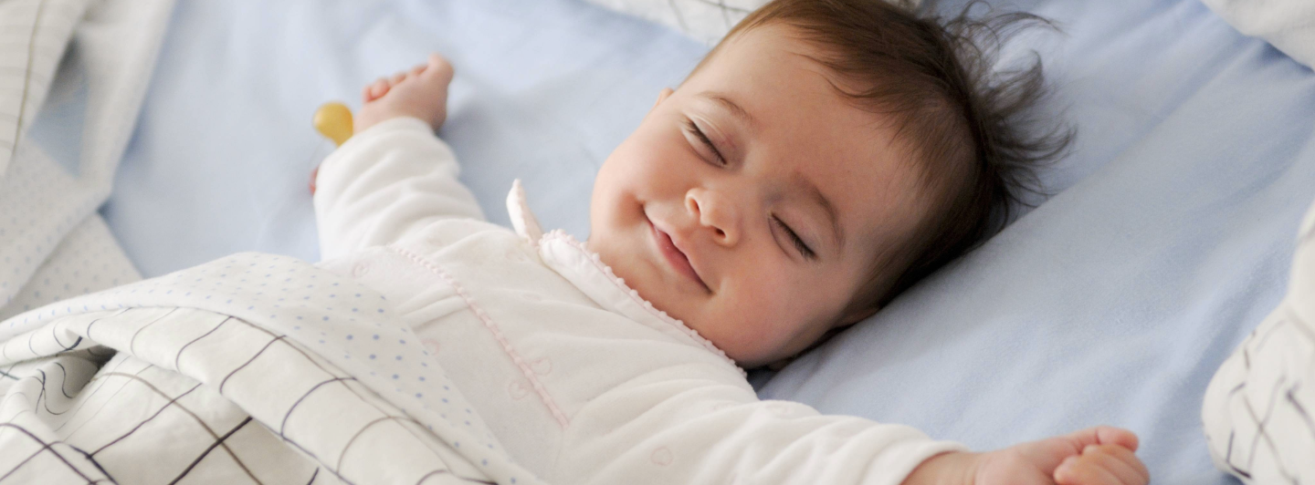 Bebé sonriendo mientras duerme plácidamente, simbolizando bienestar y desarrollo saludable durante la infancia.