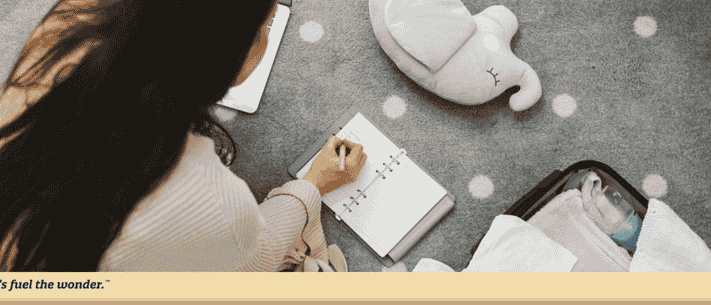 Woman Writing in Notebook on Polka Dot Rug Next to Laptop and Suitcase, with Slogan 'Let's Fuel the Wonder