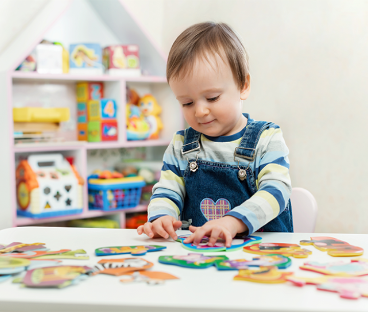 Niño pequeño juega con piezas de colores en mesa de aprendizaje, desarrollo motriz y cognitivo tras cumplir un año.