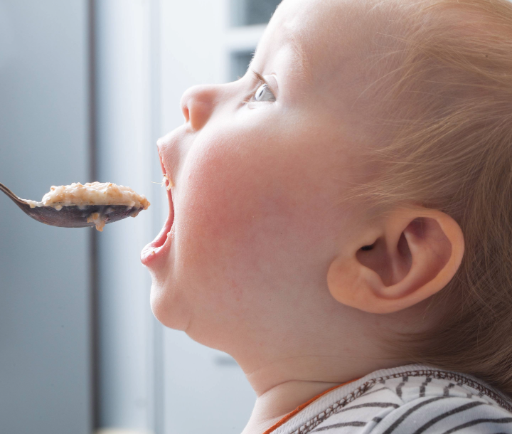 Madre alimentando con cuchara a su bebé de cinco meses, junto a texto sobre la importancia de mantener horarios en la alimentación infantil.