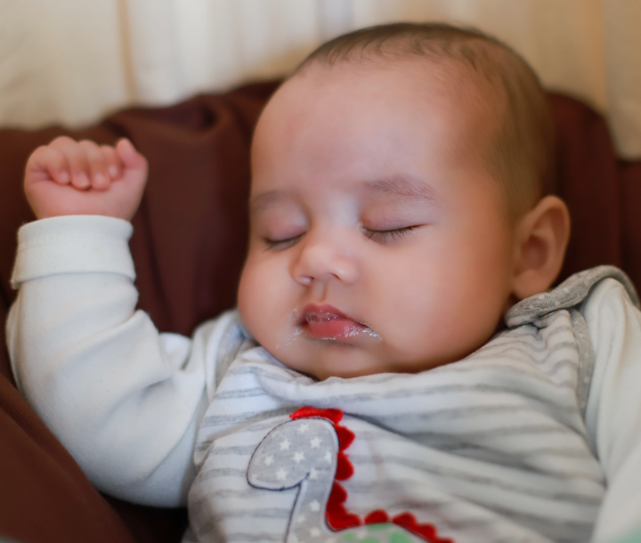 Bebé con restos de leche en la boca tras regurgitar, acompañado de texto sobre la normalidad de la regurgitación y el reflujo en bebés.