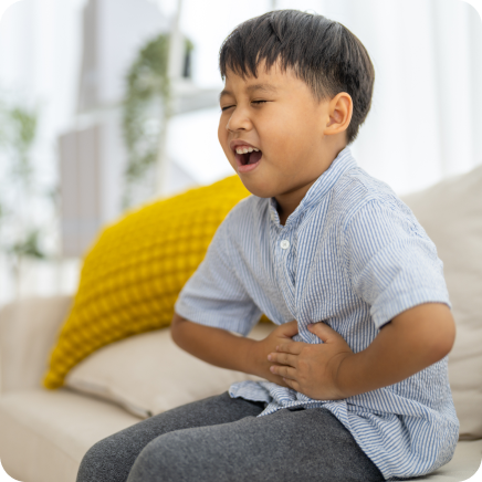 Young Boy Experiencing Stomach Pain As He Sits On Sofa