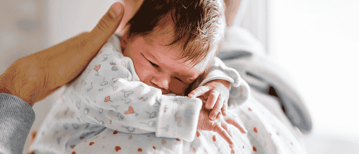 Baby in White Outfit with Heart and Tree Design, Held by Adult with Hands on Baby's Head