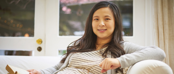 Pregnant woman sitting on sofa with book on one hand