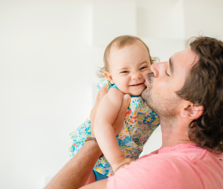 Padre cargando y besando a su bebé, importancia del rol paterno en la lactancia materna.