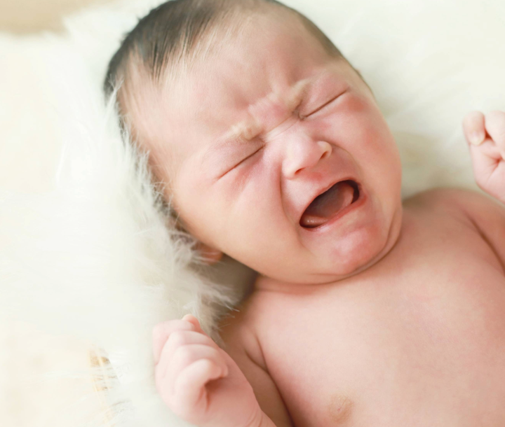 Bebé acostado llorando con molestias, representando síntomas de estreñimiento o diarrea infantil.