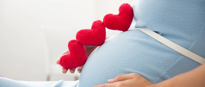 Close-up of pregnant belly with three heart-shaped plushies 
