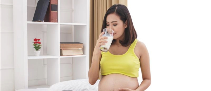 Pregnant woman drinking a glass of fresh milk at home while sitting