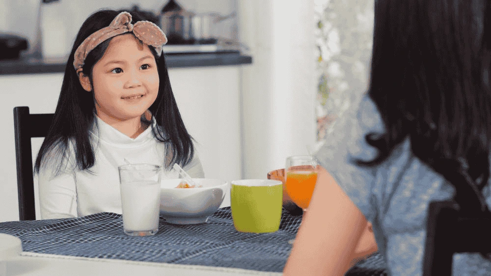 A Young Child Eating Healthy Food, Smiling While Looking At Her Mom