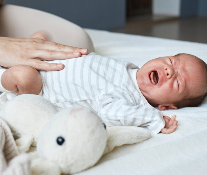 Bebé llorando mientras recibe consuelo, mostrando irritabilidad, cólicos y gases comunes en los primeros meses.