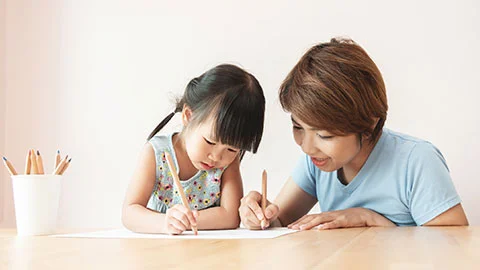 A Mother Helping Her Young Child Draw While Sitting Together At A Table