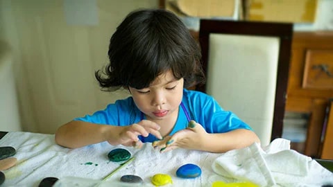 A Young Child Painting With Colorful Paints On A Table Indoors