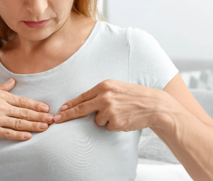 Mujer tocando su pecho con dolor, ilustrando síntomas de mastitis durante la lactancia y la importancia del tratamiento adecuado.