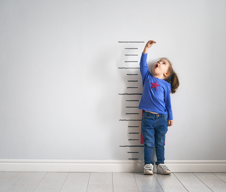 Niño mide su estatura en una pared con regla de crecimiento, representando el desarrollo físico infantil.
