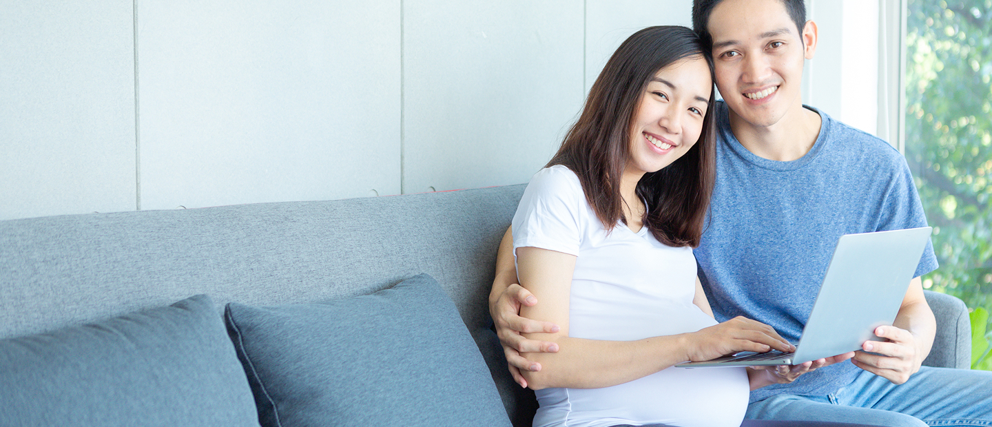 Expectant Parents Looking At Laptop On Couch