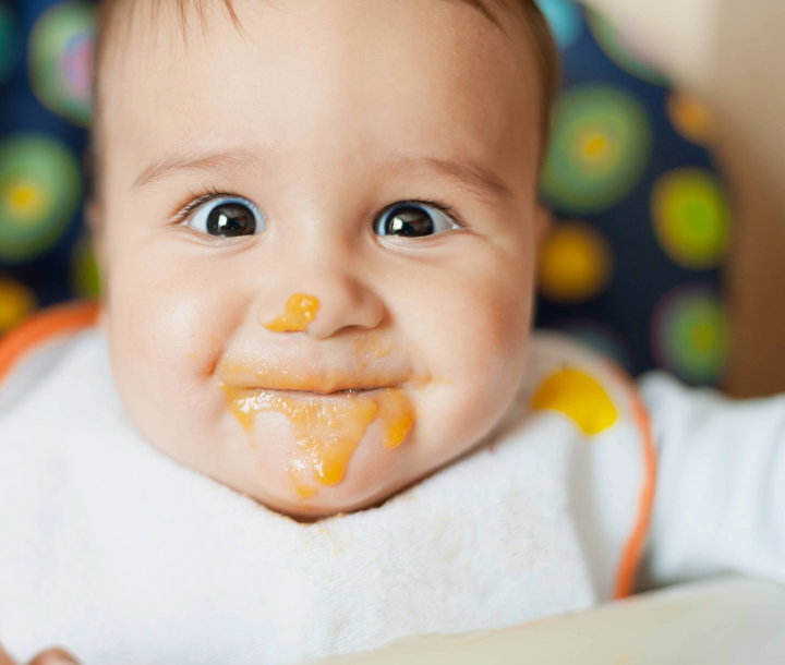 Bebé comiendo papilla de color naranja, resaltando la importancia del hierro en la dieta infantil.