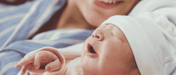 Mother Holding Sleeping Baby with White Cap, Both with Light Pink Skin Tone