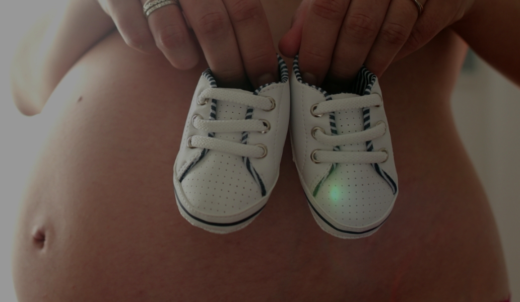 Mujer embarazada sosteniendo medias sobre su barriga, representando ilusión y preparación para la llegada del bebé.
