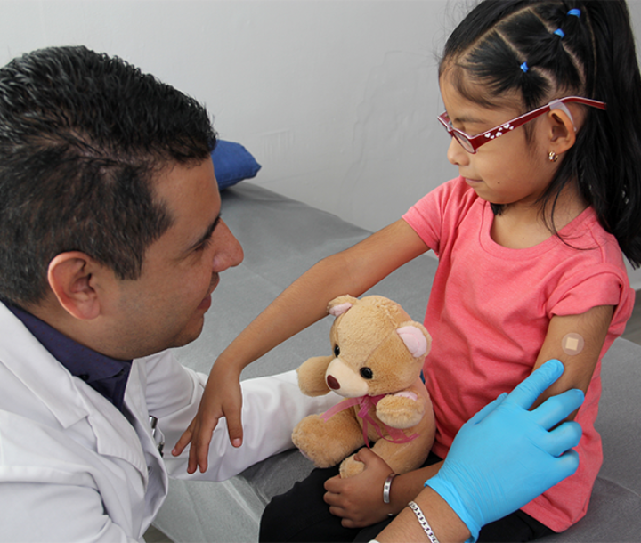 Pediatra revisando a una niña pequeña con un estetoscopio mientras ella sostiene un peluche, ilustrando la detección de la anemia.