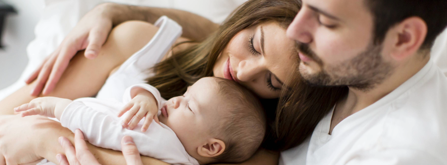 Padres acostados junto a su bebé recién nacido, mostrando amor, unión familiar y desarrollo en los primeros días de vida.